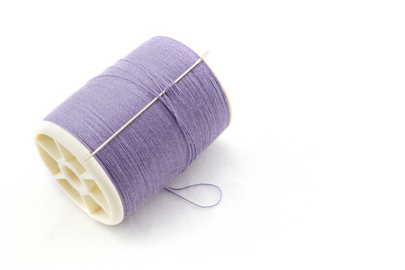 Spool of purple thread and needle on white background