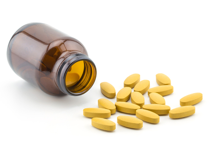 Pills of vitamin C spilled out open container on white background.の写真素材