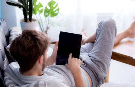 Happy man watching media content in a tablet sitting on a couch at home - Top side view mock up.の写真素材