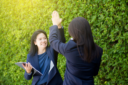 Businesswoman two people high fiving outdoors nature background.の写真素材