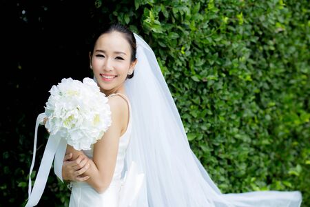 beautiful young woman on wedding day in white dress in the tree wall. Female portrait in the park -...