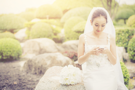 bride touch on phone in wedding dress on garden.の写真素材