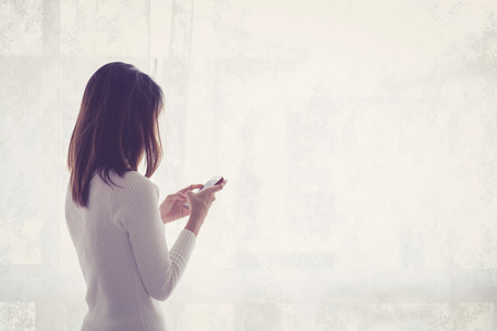 Beautiful young woman asian behind holding phone at a window.の写真素材