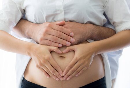 Pregnant belly with hand heart symbol. Beautiful Young Pregnant woman and husband together pregnancy - Love Concept.の写真素材