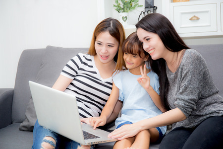 Mother, Aunt and kid having time together lerning with using laptop at home on couch, family concept.の写真素材