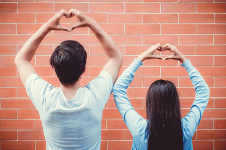 Young asian couple happy in love with gesture hand heart shape on brick background.の写真素材