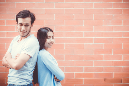 Young couple asian attractive looking face and smiling while standing back to back against brick wall with romantic.の写真素材