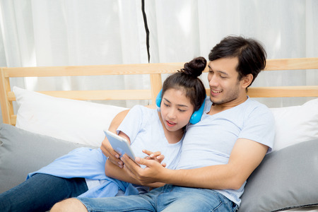 Beautiful asian young couple listening to music with tablet on bed, Love, dating,Young couple in sitting together in bed using a Tablet.の写真素材