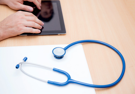 male doctor with tablet computer and stethoscope at the deskの写真素材