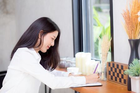 Beautiful business asian young woman writing on notebook on table, girl work at coffee shop, freelance business concept.の写真素材