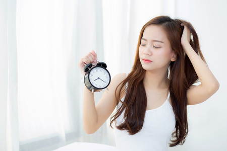 Beautiful asian young woman wake up in morning annoyed alarm clock holding hand, girl hurry wake late with appointment, lifestyle concept.の写真素材