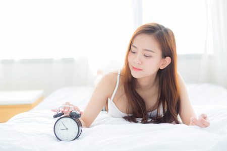 Beautiful asian young woman turn off alarm clock in morning, wake up for sleep with alarm clock, relax and lifestyle concept.の写真素材