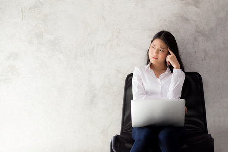 Beautiful young asian woman working and thinking with problem to stress and unhappy, businesswoman with laptop computer on cement background with emotion, freelance business concept.の写真素材