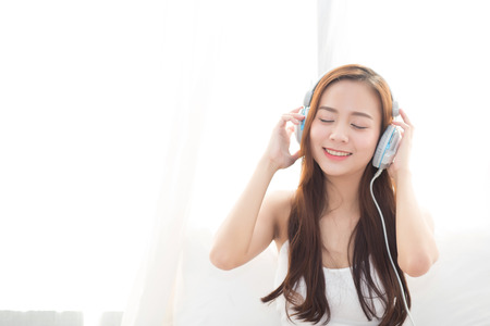 Beautiful asian young woman enjoy listen music with headphone while sitting in bedroom, relax girl with earphone internet online, leisure and technology concept.の写真素材