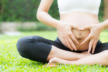 Happy pregnant beautiful young woman with gesture hand heart shape in the park, closeup woman with...