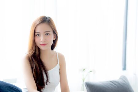 Beautiful young asian woman sitting the window and smile while wake up with sunrise at morning, lifestyle and relax concept.の写真素材