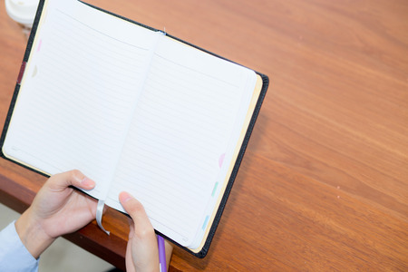 closeup woman hand writing on notebook on wooden table, girl work with paper at coffee shop, top...