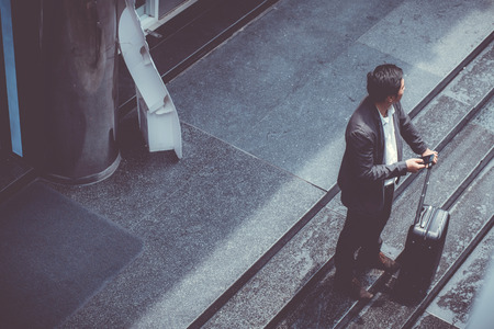 Asian elegant businessman wear suit talking mobile phone while walking holding suitcase outdoor on street, young man contact with customer appointment, communication business concept.の写真素材