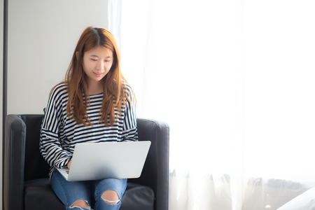 Beautiful of portrait young asian woman using laptop computer  for leisure on chair at living room, girl working online with notebook freelance, communication business concept.の写真素材
