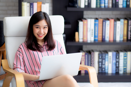 Beautiful of portrait asian young woman freelance working online laptop sitting on chair at living room, girl using notebook computer with connect to internet for distance job, business and success concept.の写真素材