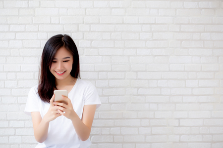 Beautiful of portrait young asian woman touch phone and smile standing on cement brick background, freelance female calling telephone, communication concept.の写真素材
