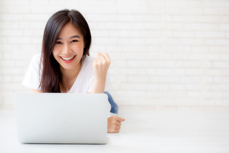 Beautiful of portrait asian young woman excited and glad of success with laptop computer, girl lying working on cement brick background, career freelance business concept.の写真素材
