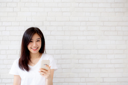 Beautiful of portrait young asian woman touch phone and smile standing on cement brick background, freelance female calling telephone, communication concept.の写真素材