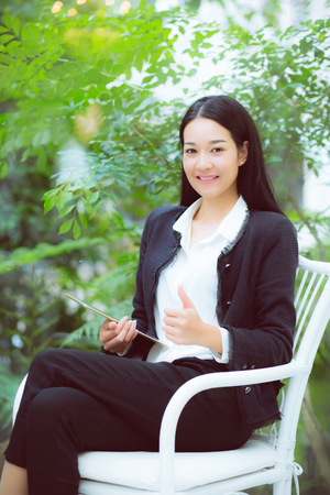 Beautiful portrait business young asian woman smile and happy sitting using digital tablet computer work at home, businesswoman on chair gesture excellent sign, communication concept.の写真素材