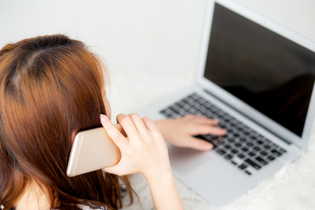 Beautiful asian young woman lying on bed using laptop and talking mobile smart phone at bedroom for leisure and relax, freelance with girl working notebook, communication concept, top view.の写真素材