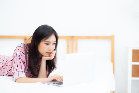Beautiful asian young woman lying on bed using laptop at bedroom for leisure and relax, freelance with girl working notebook, communication concept.の写真素材