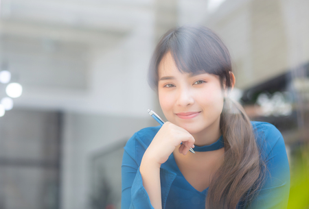 Beautiful portrait young asian woman writer smiling thinking idea and writing on notebook or diary with happy, lifestyle of asian girl is student, female planning working, education and business concept.の写真素材