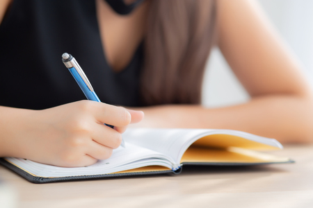 Closeup hand asian woman sitting study and learning writing notebook and diary on table in living room at home, girl homework, business writer woman working on table, education concept.の写真素材