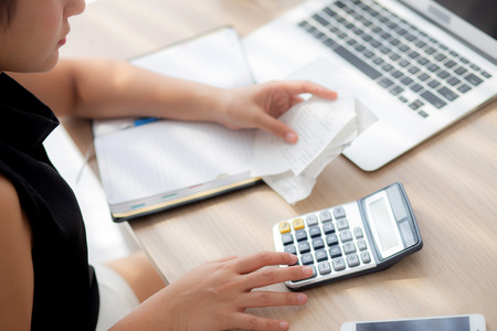 closeup hand woman calculating expenses household and writing notebook on desk, girl checking bill...
