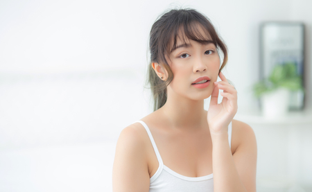 Portrait beautiful asian woman makeup of cosmetic, girl hand touch cheek and smile attractive, face beauty perfect with wellness in the bedroom at home with skin care and healthcare concept.の写真素材