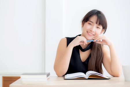 Beautiful portrait young asian woman smiling sitting study and learning writing notebook and diary in the living room at homeの写真素材