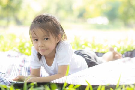 Beautiful asian child smiling using smart mobile phone in the garden, kid have passion playing game digital on smartphone on internet network in the park with happy, lifestyle and technology concept.の写真素材