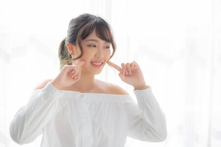 Beautiful portrait asian woman makeup of cosmetic, girl hand touch cheek and smile attractive, face beauty perfect with wellness in the bedroom with skin care and healthcare concept.の写真素材