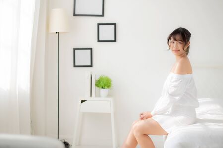 Portrait of beautiful young asian woman sitting looking the window and smile while wake up with sunrise at morning, beauty asia girl happy with freshness and cheerful, lifestyle and relax concept.の写真素材