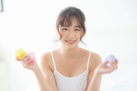 Beautiful portrait young asian woman holding and presenting cream or lotion product, beauty asia girl show cosmetic makeup and moisturizing for skin care, healthy care and wellness concept.の写真素材