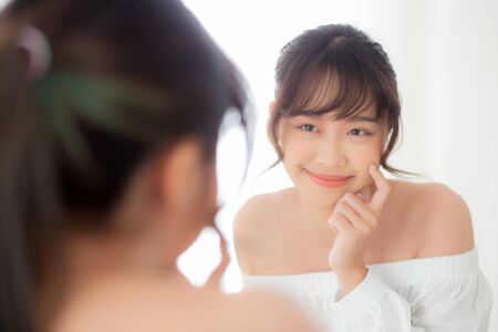 Beautiful face young asian woman with happy smiling and looking mirror, makeup of beauty facial girl with skincare and cosmetic treatment, refresh of female and clean for charming, healthy concept.の写真素材