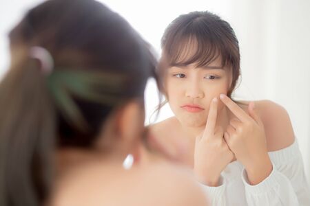 Portrait beautiful young asian woman looking the mirror is a acne, zit treatment, girl problem beauty face, perfect with wellness in the bedroom at home with skin care and  healthcare concept.の写真素材