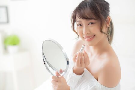 Beautiful portrait young asian woman looking mirror applying makeup lipstick at room, beauty lips asia girl makeup and cosmetic fashion on mouth at home, lifestyle and health care concept.の写真素材