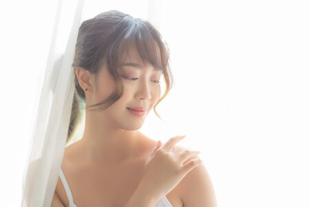 Portrait of beautiful young asian woman makeup of cosmetic, girl hand touch shoulder and smile attractive, face of beauty perfect with wellness in the bedroom with skin care and healthcare concept.の写真素材