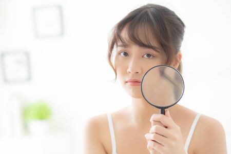 Beautiful young asian woman with magnifying of skin a problem of acne, beauty asia girl check skincare of face, female analyzing trouble, cosmetic and makeup, health and care concept.の写真素材