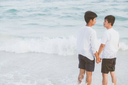 Back view homosexual young asian couple standing together on beach in summer, asia gay holding hands going sea for leisure and relax with romantic and happy in vacation at sea, LGBT with legal concept.の写真素材