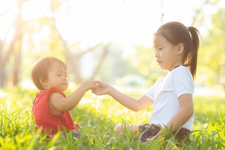 Beautiful young asian kid sitting playing in summer in the park with enjoy and cheerful on green grass, children activity with relax and happiness together on meadow, family and holiday concept.の写真素材