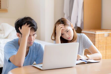 Young asian couple stressed and worried about finance of problem business together, man and woman looking laptop and frustrated, family unhappy and depression about debt, lifestyle concept.の写真素材