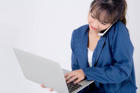 Beautiful portrait young asian business woman holding laptop computer and talking smart mobile phone isolated on white background, model businesswoman using notebook, communication concept.の写真素材