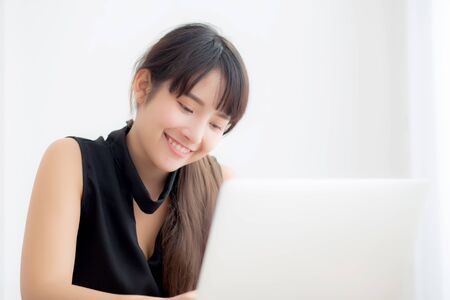Beautiful young freelance asian woman smiling working and typing on laptop computer at desk office with professional, girl using notebook checking email or social network, business and lifestyle concept.の写真素材