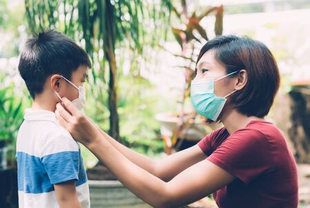 Mother take care son with face mask for protection disease flu or covid-19 outdoors, mom wearing on medical mask with child safety for protect outbreak of pandemic in public, medical concept.の写真素材